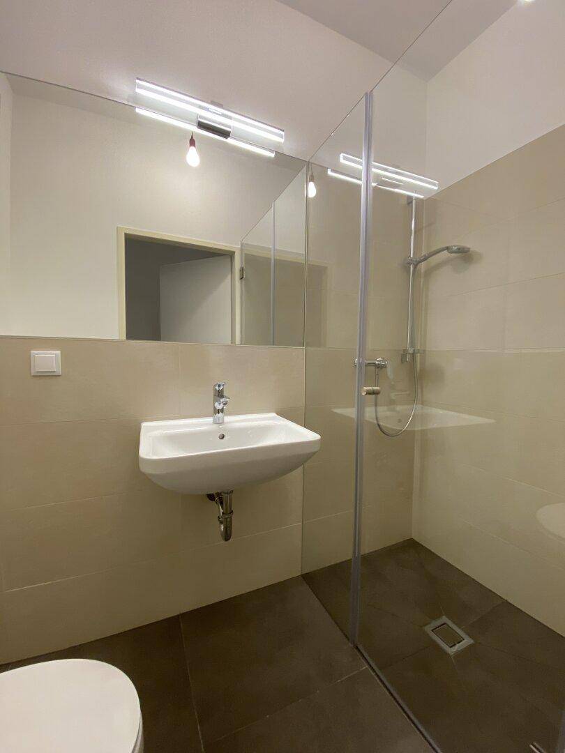 Modernes Badezimmer mit begehbarer Dusche, Wandspiegel und beigefarbenen Fliesen.