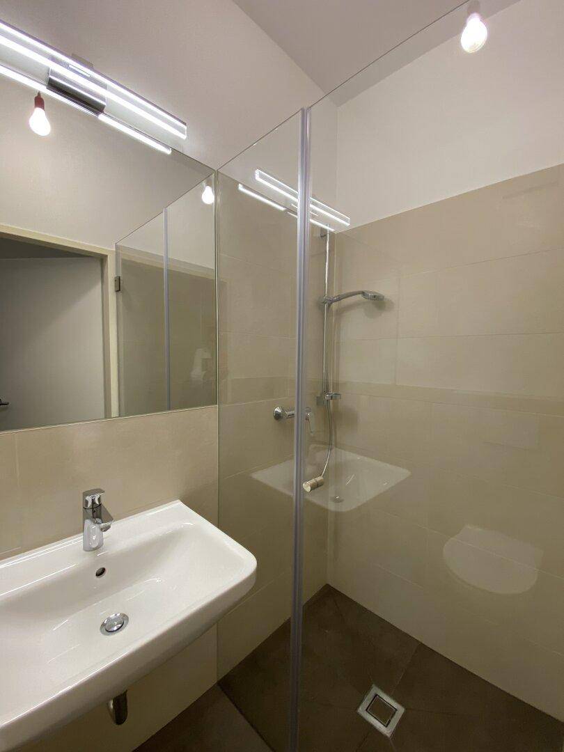 Helles Badezimmer mit begehbarer Dusche, modernem Waschbecken und großen Wandspiegeln.
