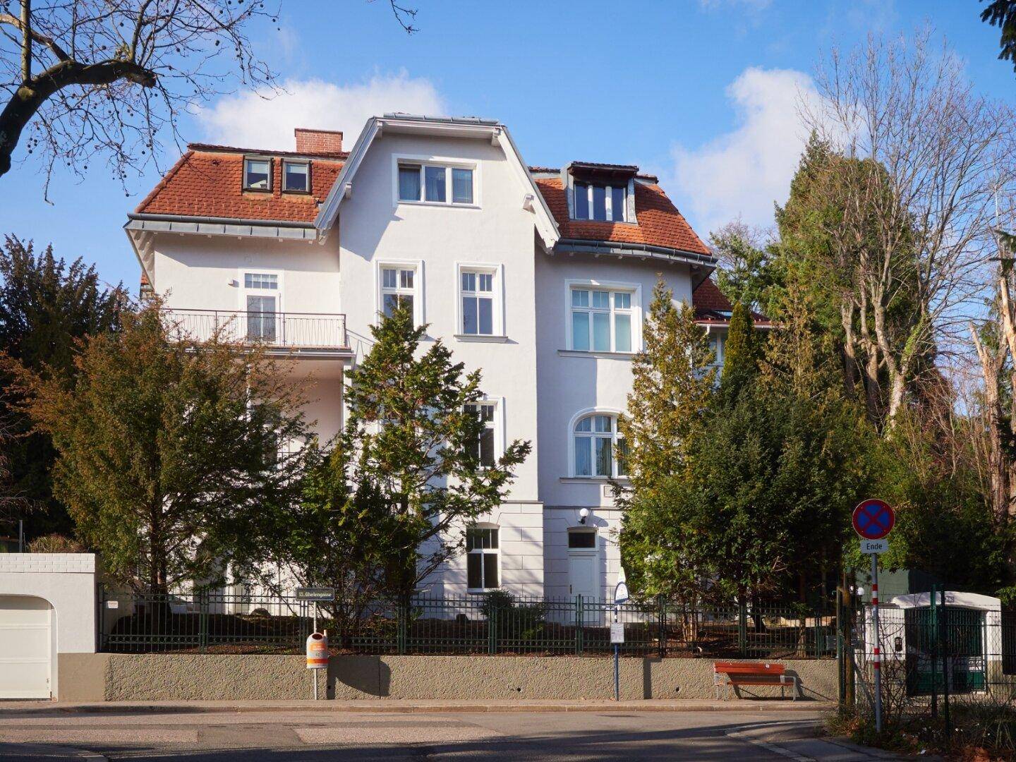 Elegante Stadtvilla mit weißer Fassade, roten Dächern und Balkonen.