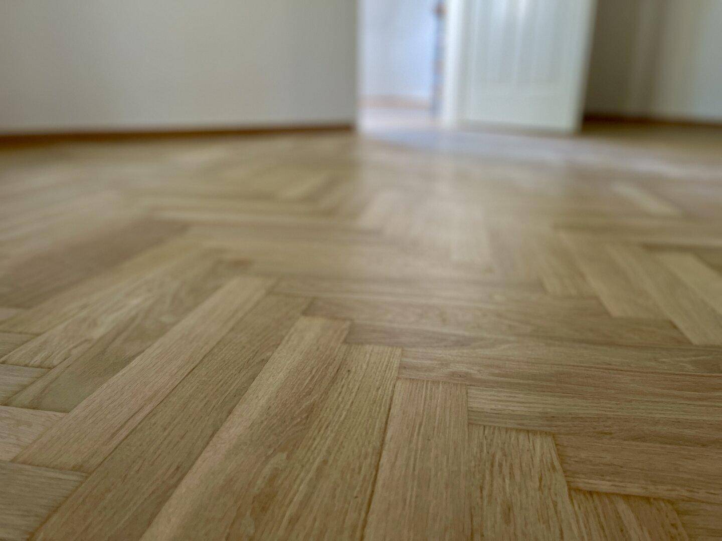 Nahaufnahme eines Fischgrätparkettbodens aus hellem Holz.