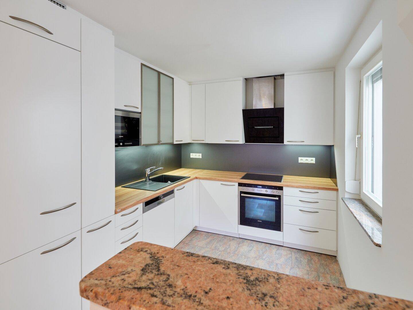 Moderne Einbauküche mit weißen Fronten, Holz-Arbeitsplatte und Granit-Theke.