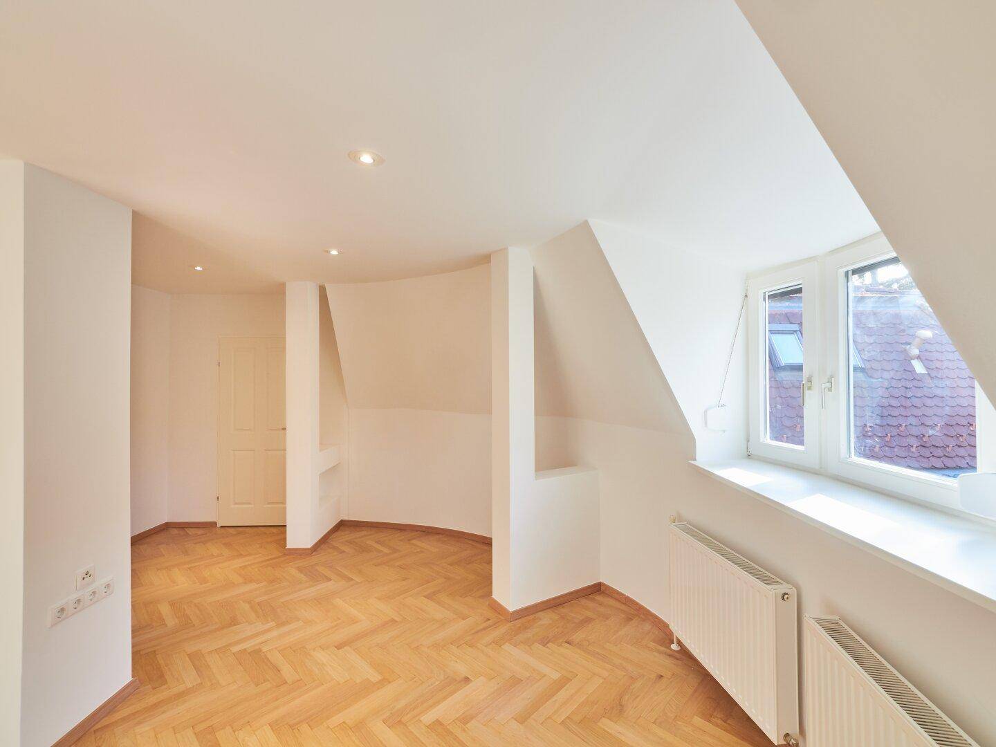 Helles Zimmer mit Parkettboden, Dachschrägen und Einbaunischen.