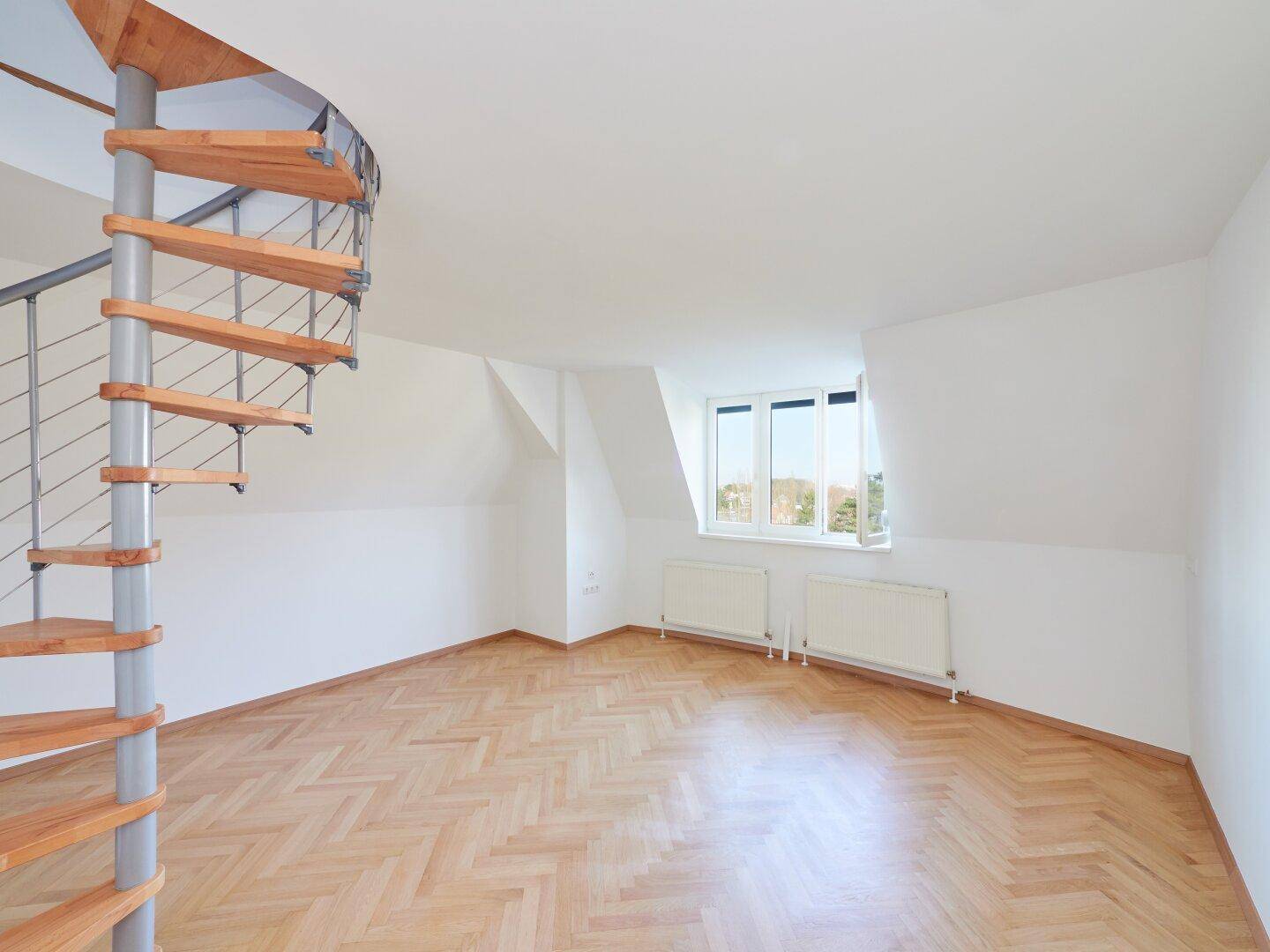 Helles Zimmer mit Wendeltreppe, Fischgrätparkett und Dachschrägenfenstern.