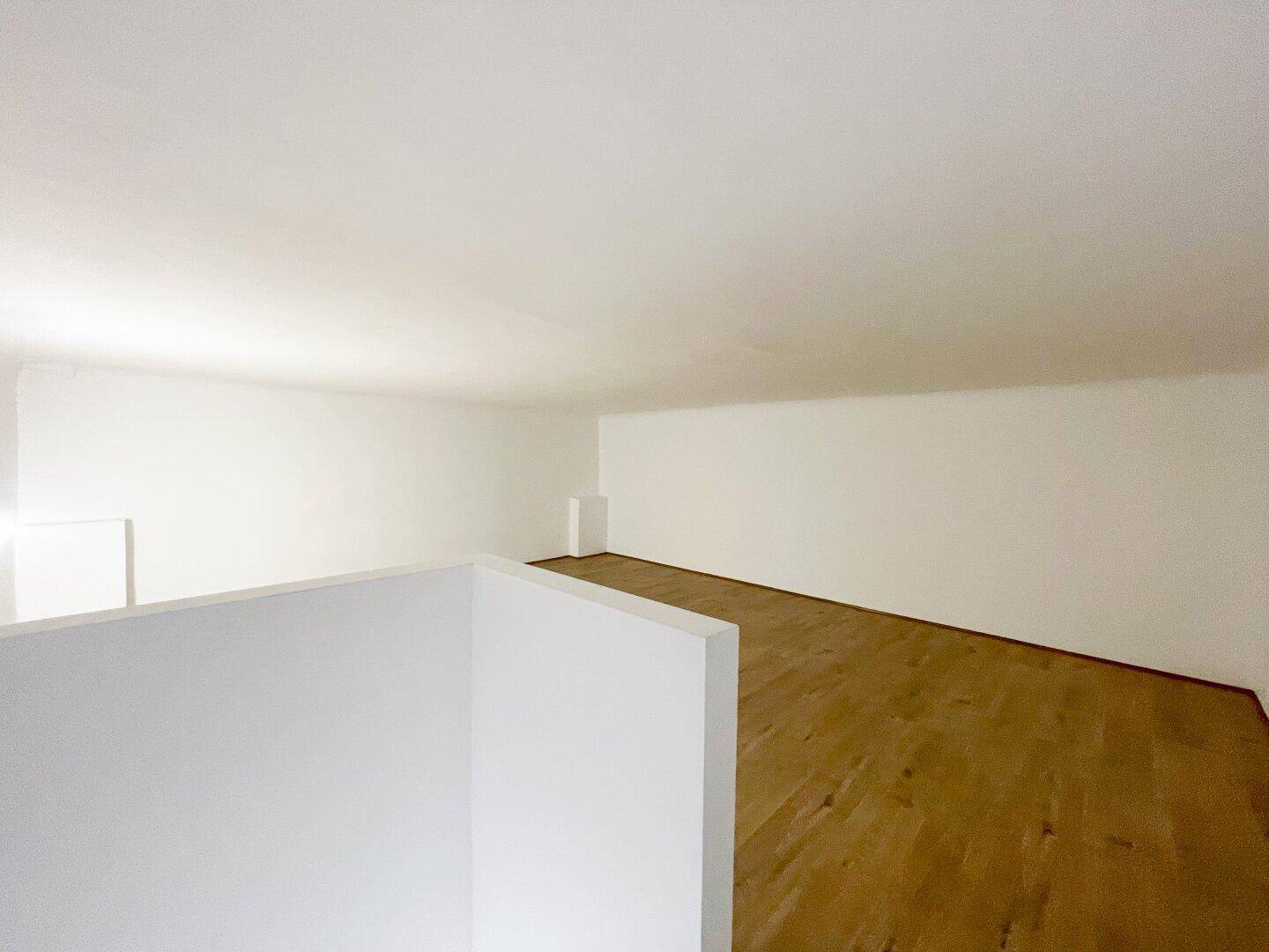 Obergeschoss eines Geschäftsraums mit hellem Holzboden und schlichten weißen Wänden, ideal für Büro oder Lager.