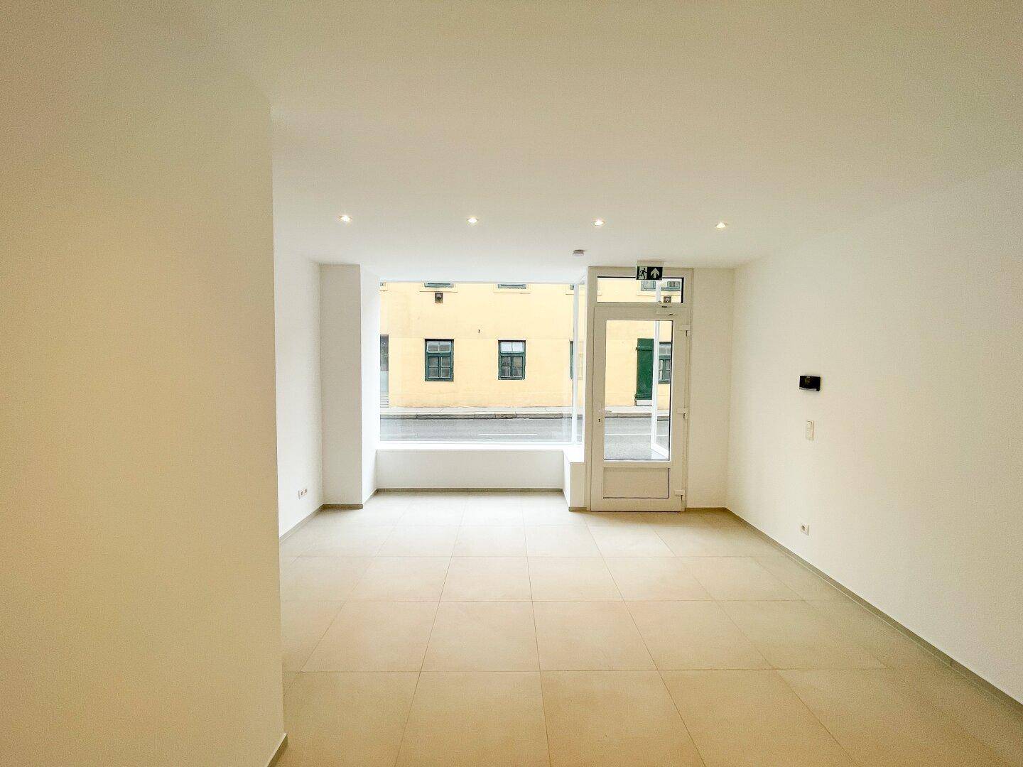 Geräumiger, heller Geschäftsraum im Erdgeschoss mit großen Fenstern zur Straße und einem pflegeleichten Fliesenboden.