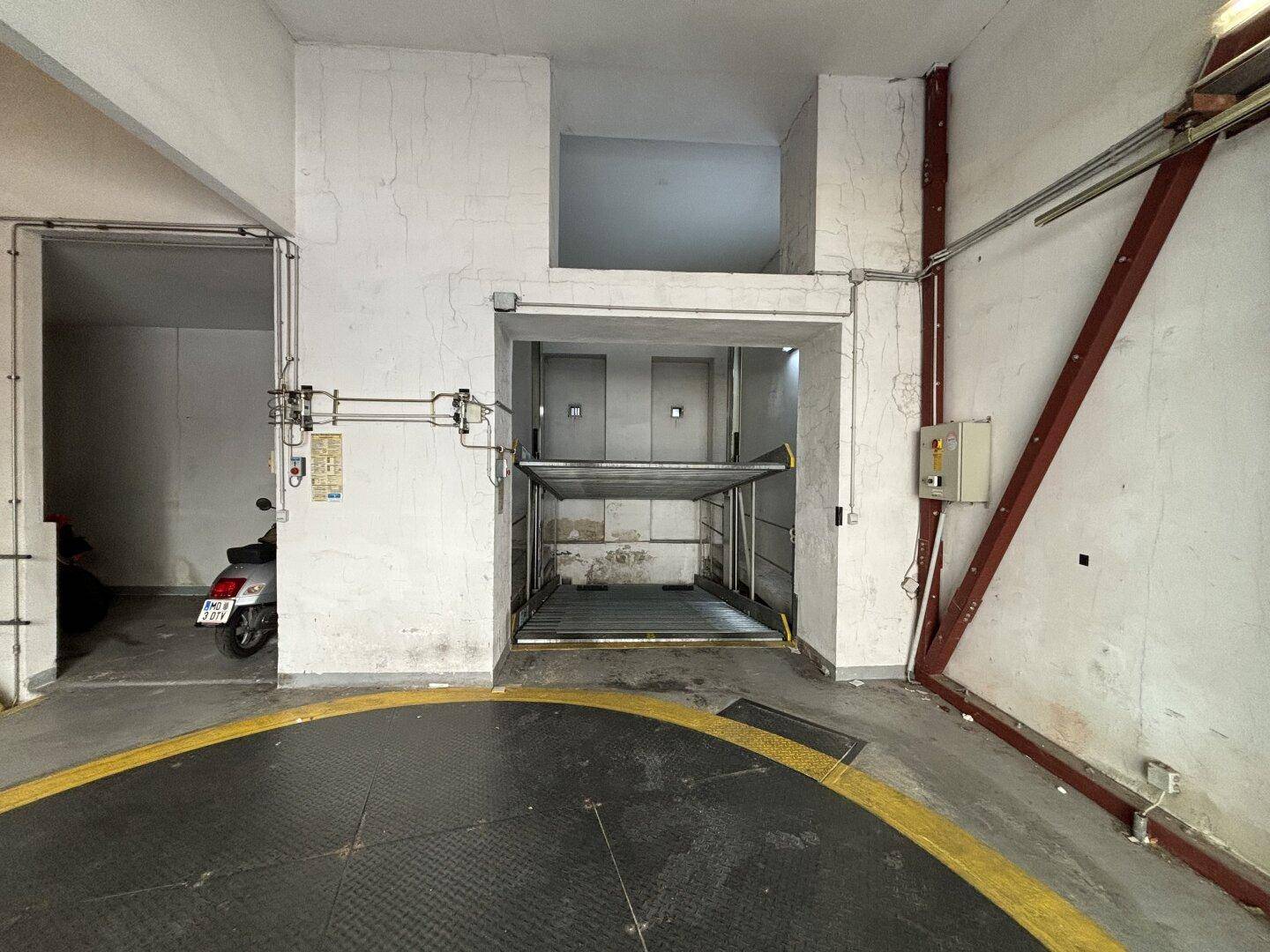 Tiefgarage mit einem leeren automatischen Parksystem und einem Roller an der Seite, helle Wände.