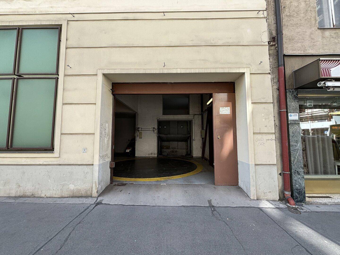 Eingang zur Tiefgarage von der Straße aus gesehen, mit einem großen Tor und Gebäudefassade.