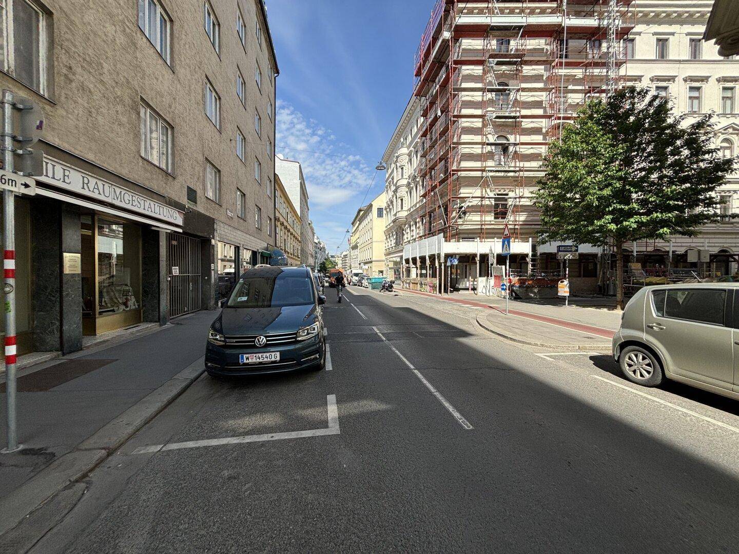 Eine belebte Stadtstraße mit geparkten Autos und einem Gebäude unter Gerüst auf der rechten Seite.