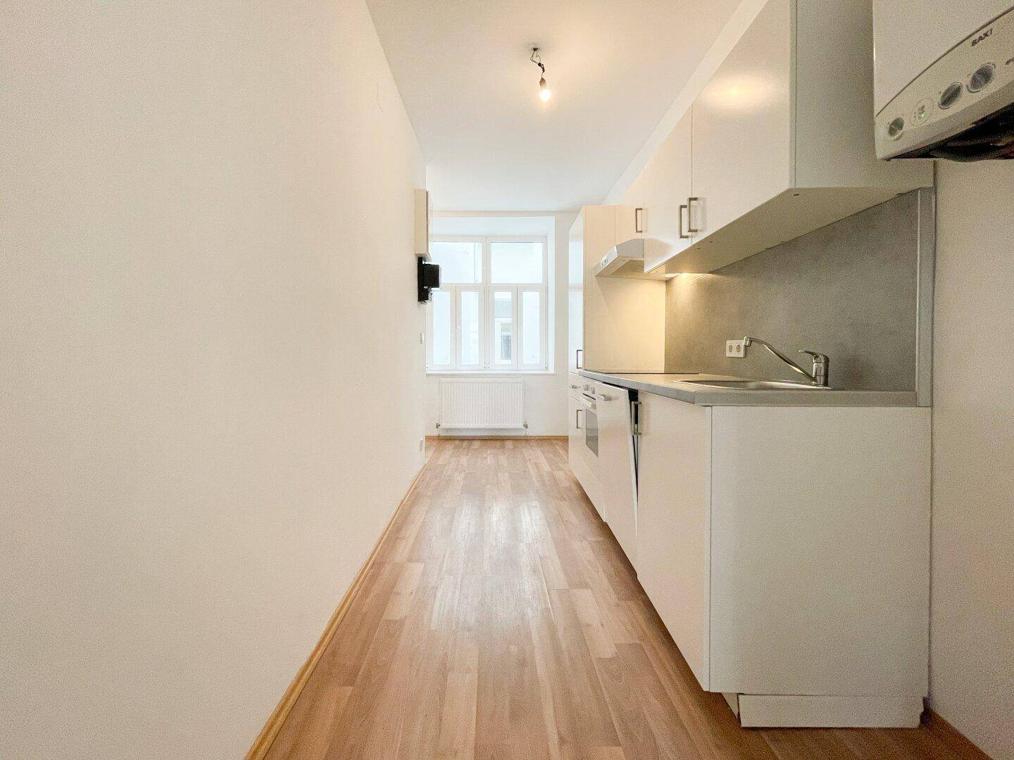 Helle, schmale Küche mit weißen Einbauschränken und Fenster am Ende des Raumes.