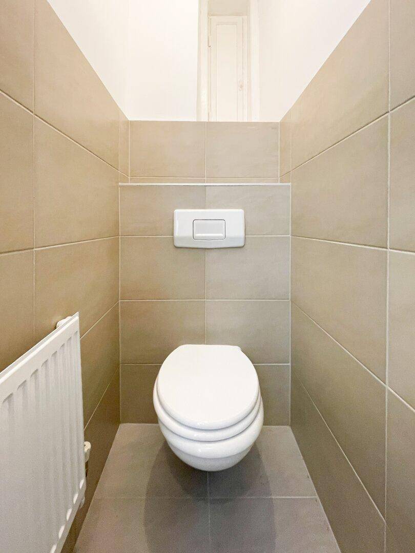Separate Toilette mit beigefarbenen Wandfliesen und einem modernen wandhängenden WC.