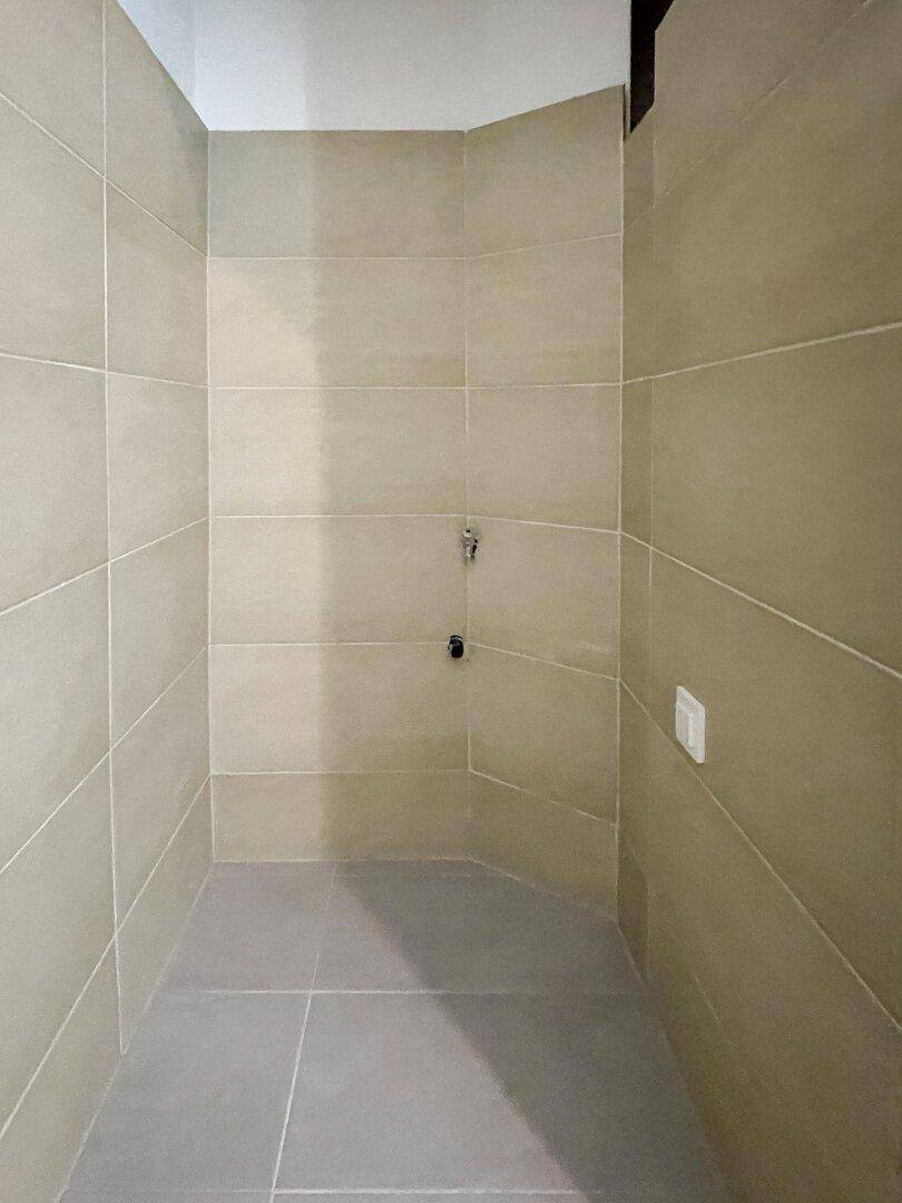 Duschbereich mit beigefarbenen Wandfliesen und grauen Bodenfliesen, bereit für die Installation einer Dusche.