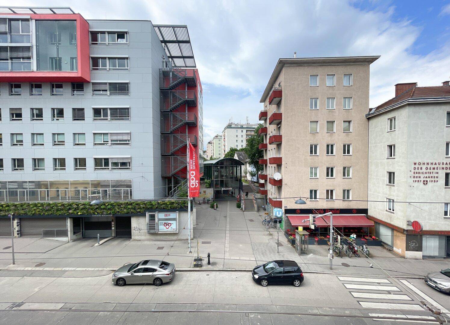 Blick auf eine belebte Stadtstraße mit modernen und älteren Gebäuden sowie parkenden Autos.