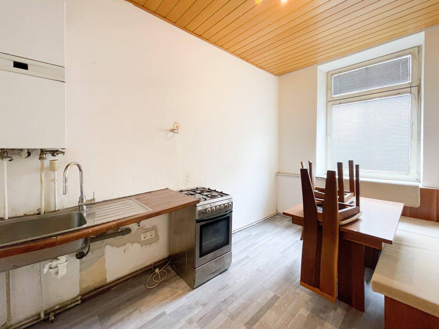 Funktionale Küche mit Gasherd, Spüle und einem Essbereich mit Holztisch und -bank.