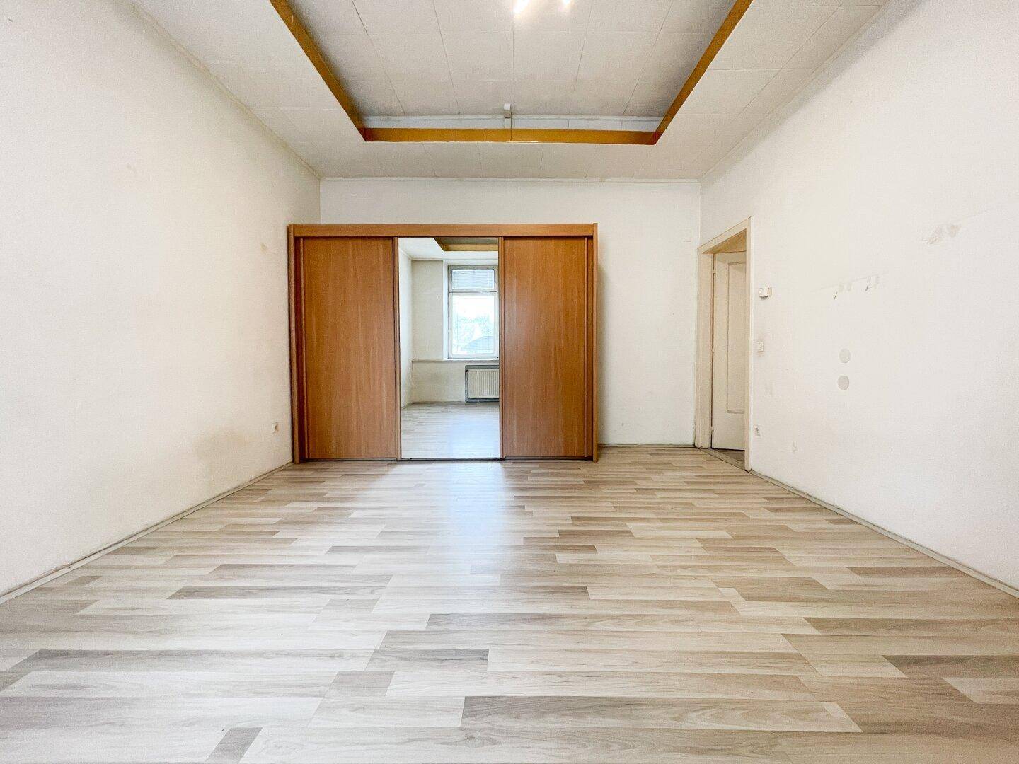 Heller Raum mit Laminatboden und großen Holzschiebetüren, die zu einem angrenzenden Zimmer führen.