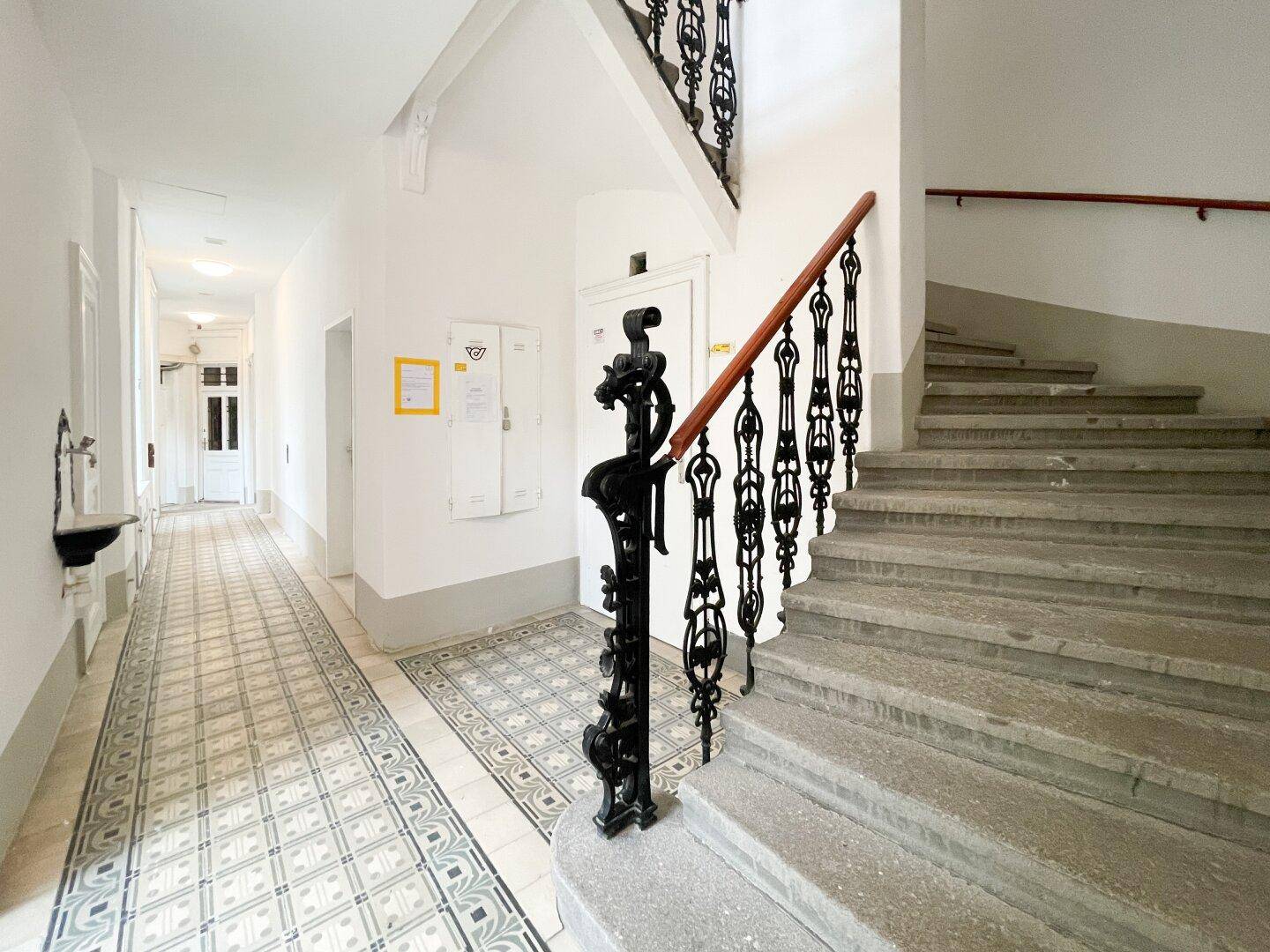 Geräumiger Flur mit historischem Treppenhaus und kunstvollem schmiedeeisernem Geländer.