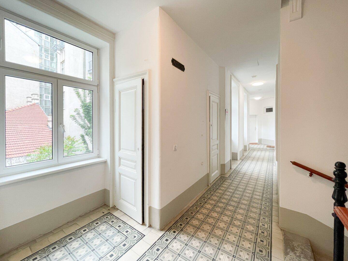 Heller Flur mit großem Fenster, das den Blick auf den Innenhof freigibt, und eleganten Türen.