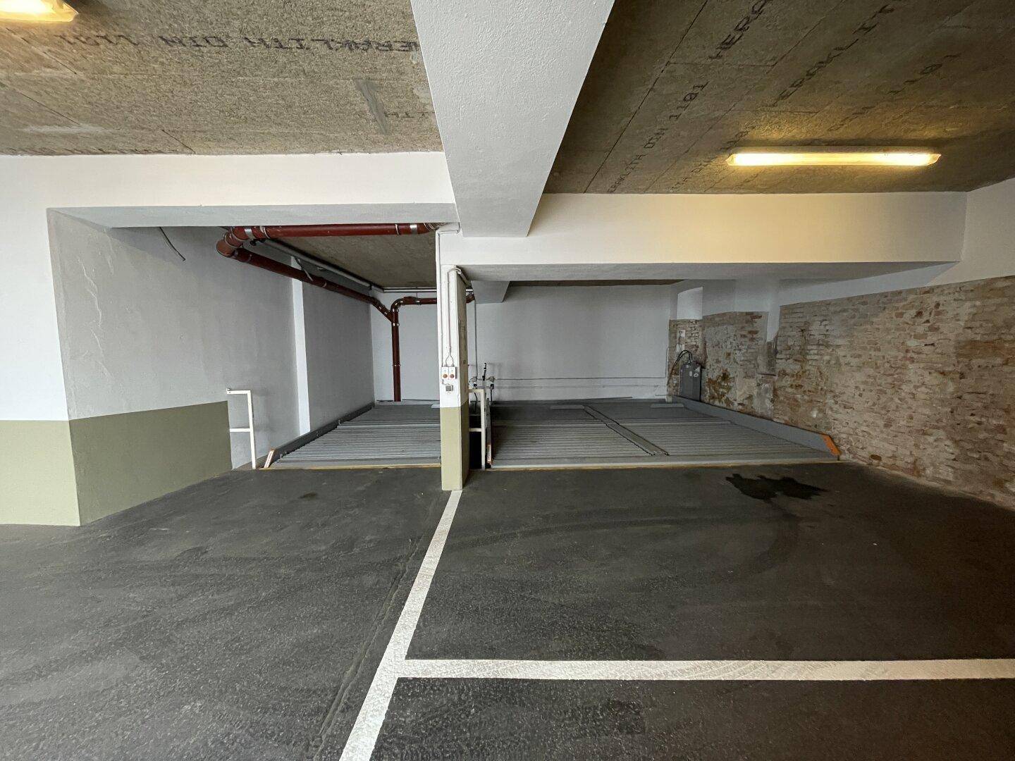 Tiefgarage mit Betonwänden, sichtbaren Rohren und markierten Parkplätzen.