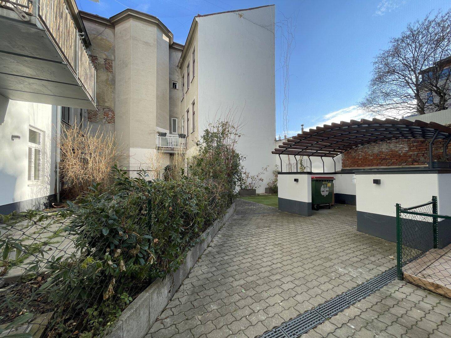 Gepflasterter Innenhof mit Grünflächen und einem Bereich für Mülltonnen.