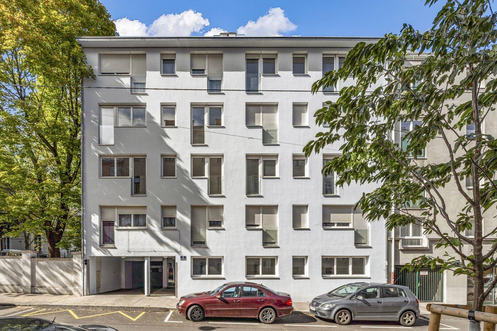 Modernes Mehrfamilienhaus mit heller Fassade, vielen Fenstern und grüner Umgebung.