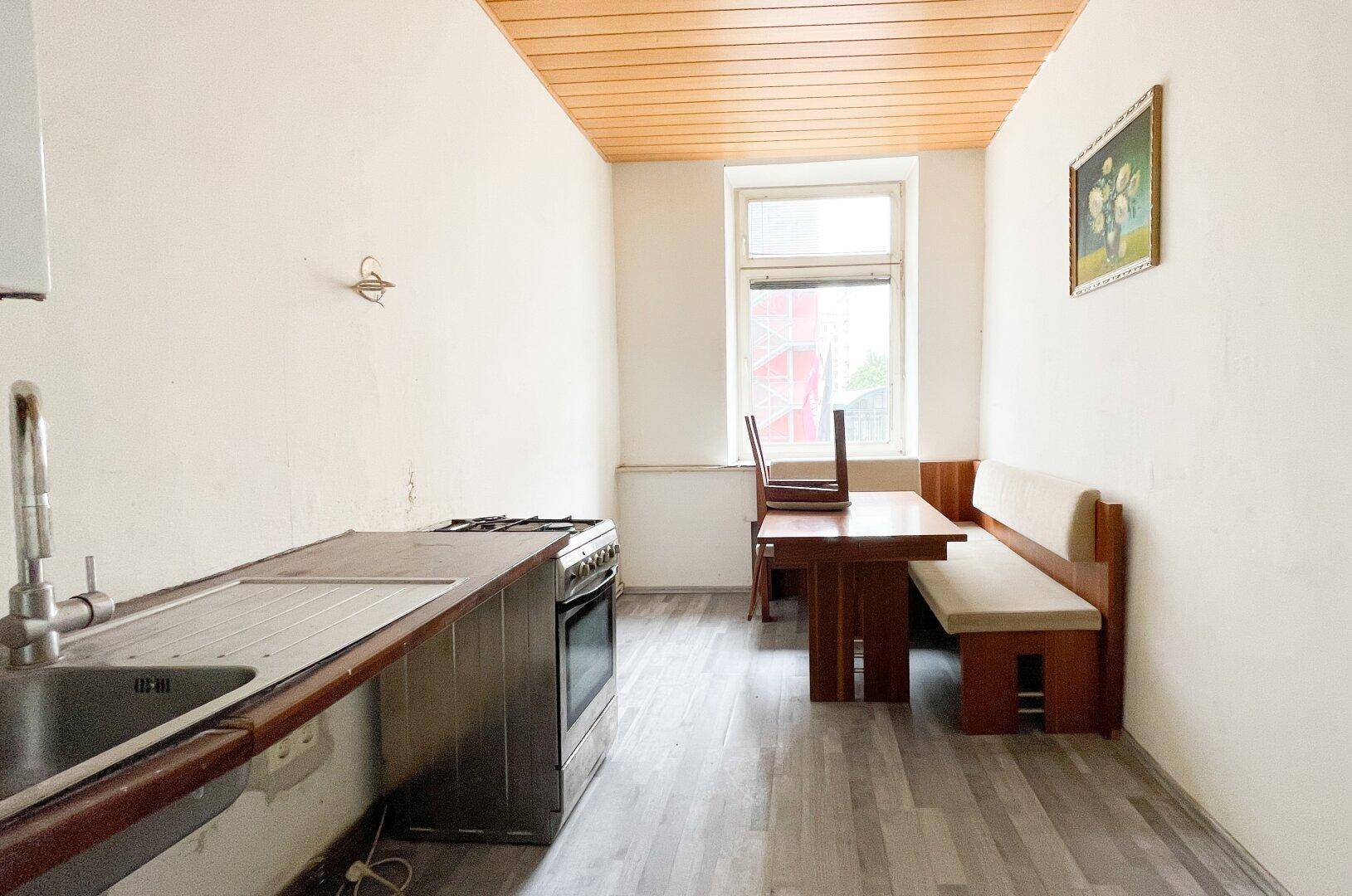 Einfache Küche mit Gasherd, Spüle und integriertem Essbereich mit Holzbank und Tisch.