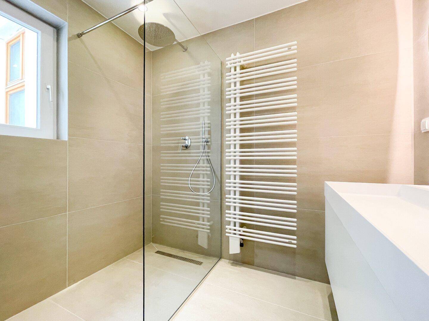 Helles Badezimmer mit Fenster, begehbarer Dusche, schwebendem Waschtisch und beheiztem Handtuchhalter.