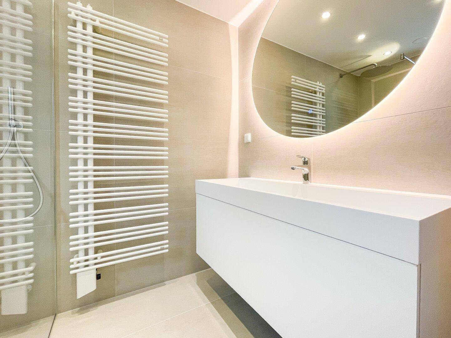 Modernes Badezimmer mit begehbarer Dusche, schwebendem Waschtisch und beleuchtetem Spiegel.
