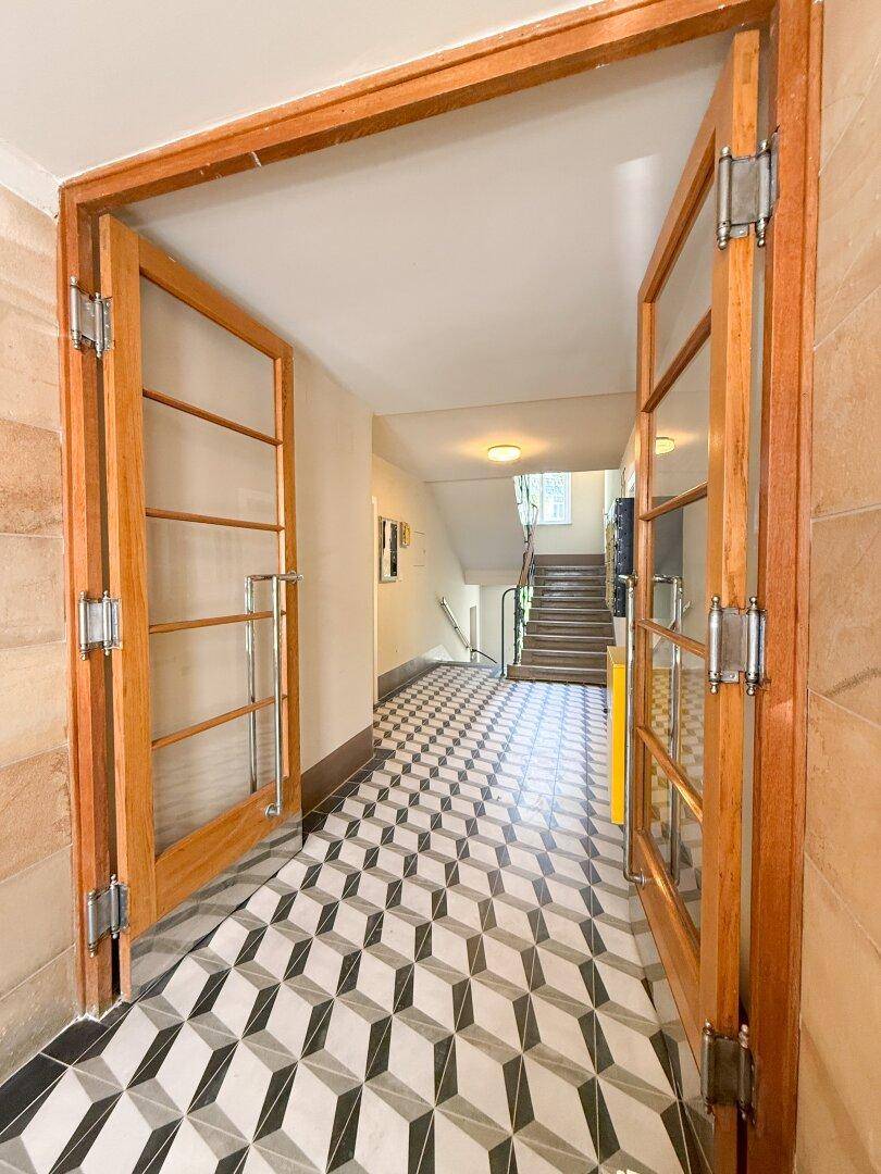 Repräsentativer Eingangsbereich mit gemusterten Fliesen und einer eleganten Holz-Glastür.