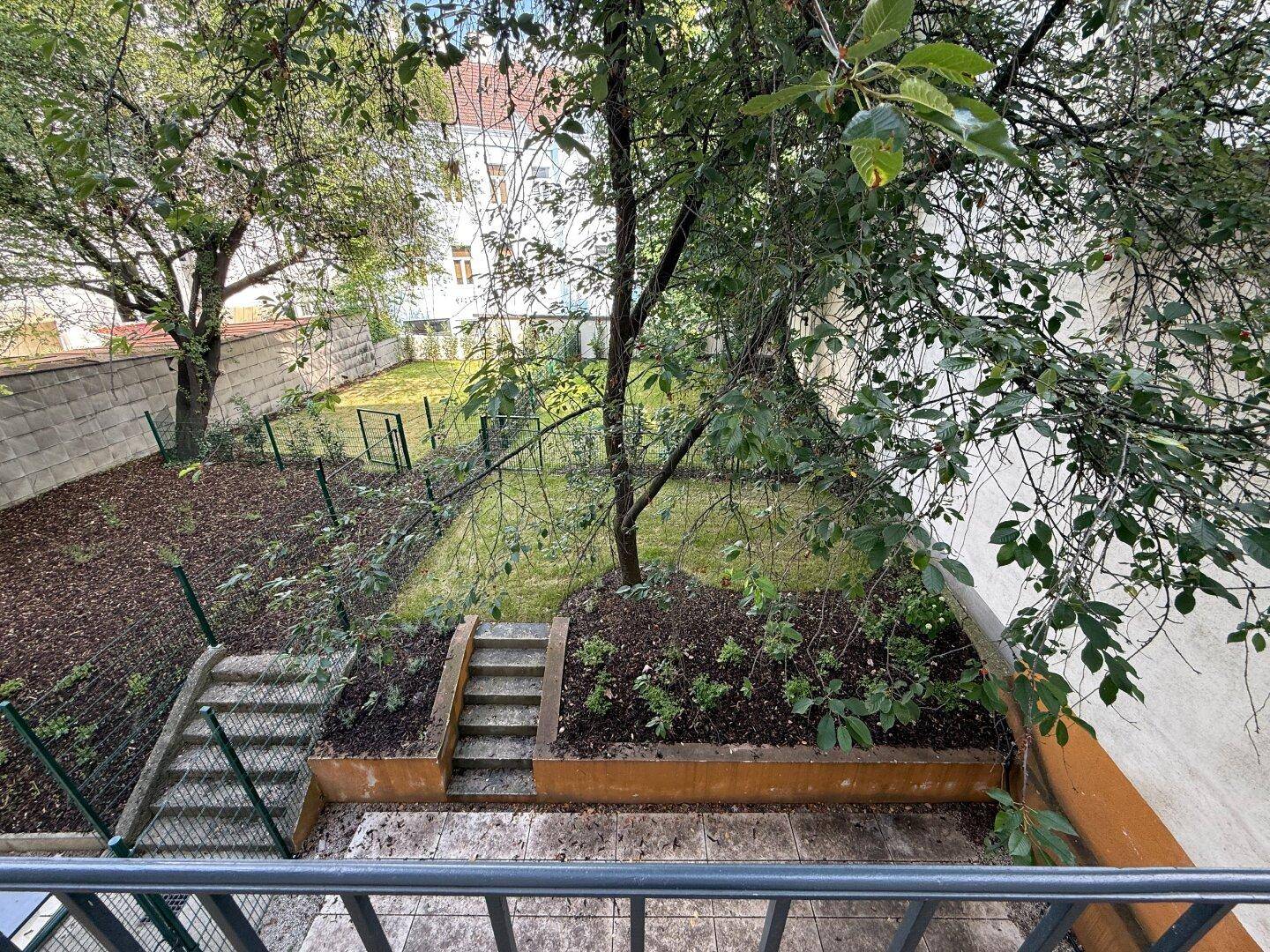 Blick von oben auf einen grünen Gartenbereich mit Bäumen und Steinstufen.