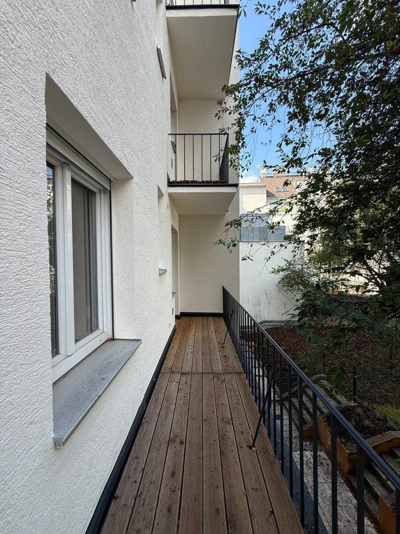 Lange Balkonfront mit Holzboden und schwarzem Geländer an der Gebäudefassade.