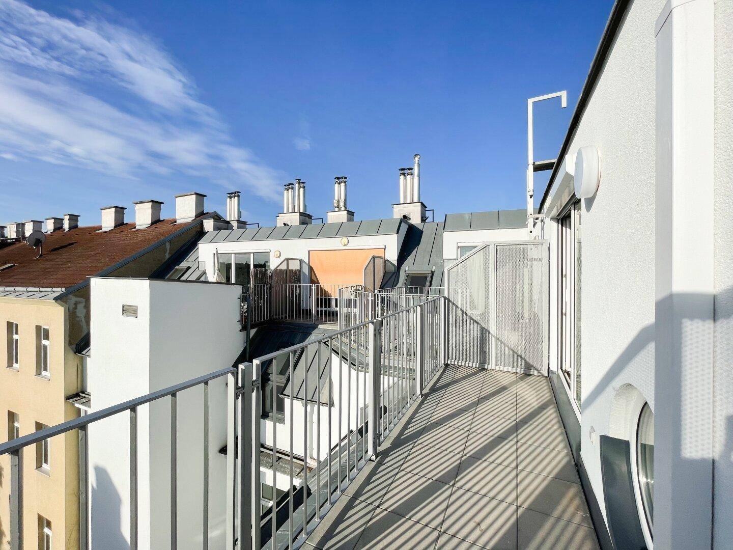 Sonniger Balkon mit Blick über die Dächer der Stadt und moderner Metallbrüstung.