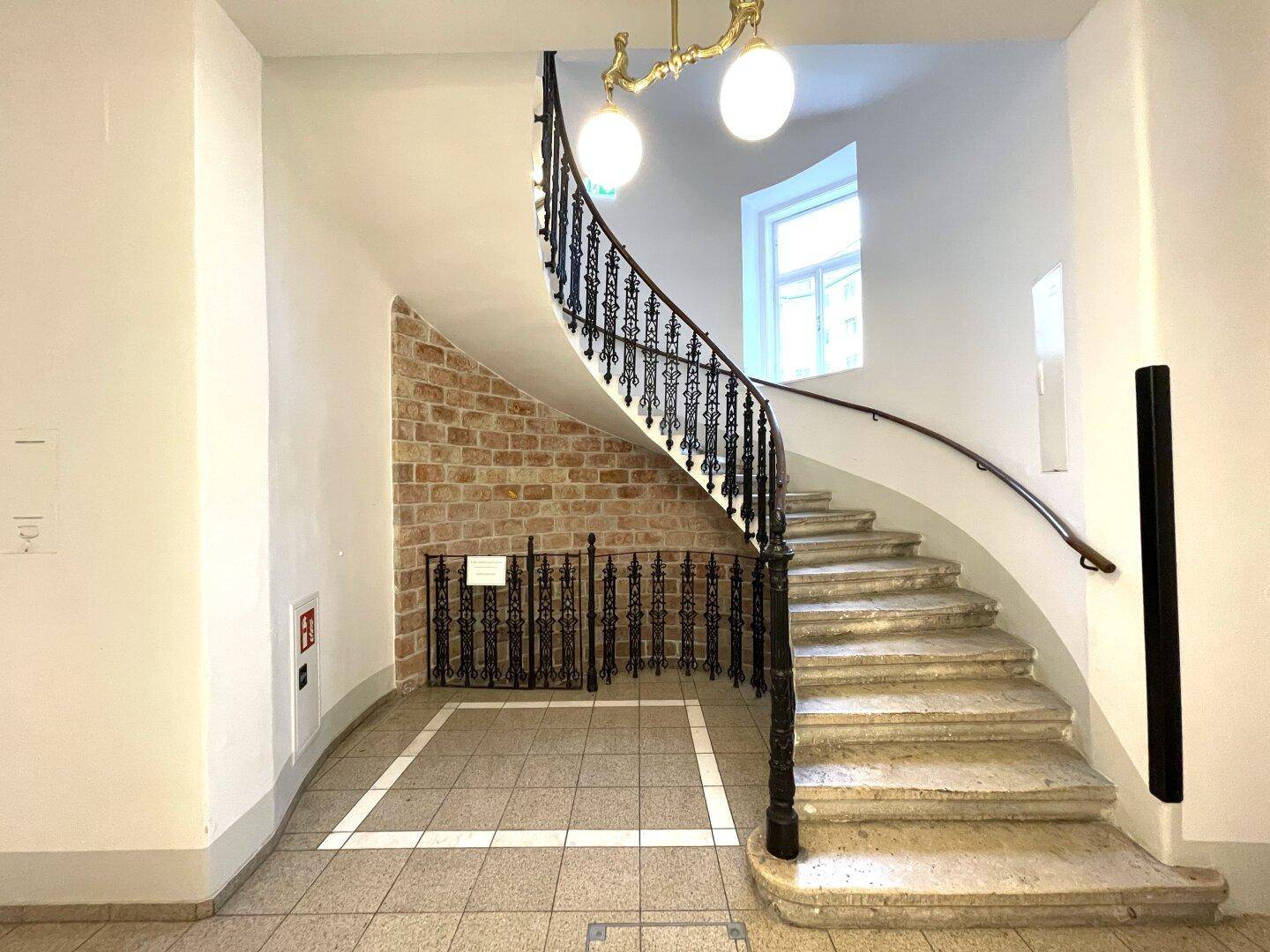 Historisches Treppenhaus mit geschwungener schmiedeeiserner Balustrade und Steinwänden.