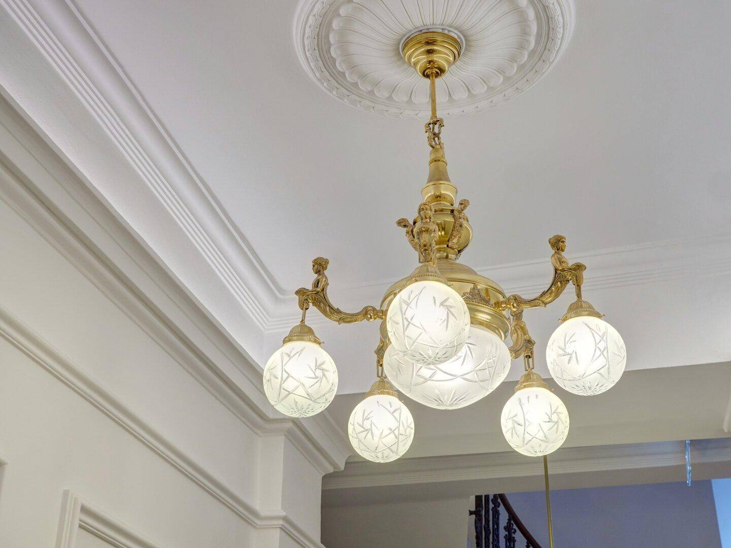 Elegante goldene Deckenleuchte mit runden Glaskugeln und aufwendiger Stuckverzierung an der Decke.