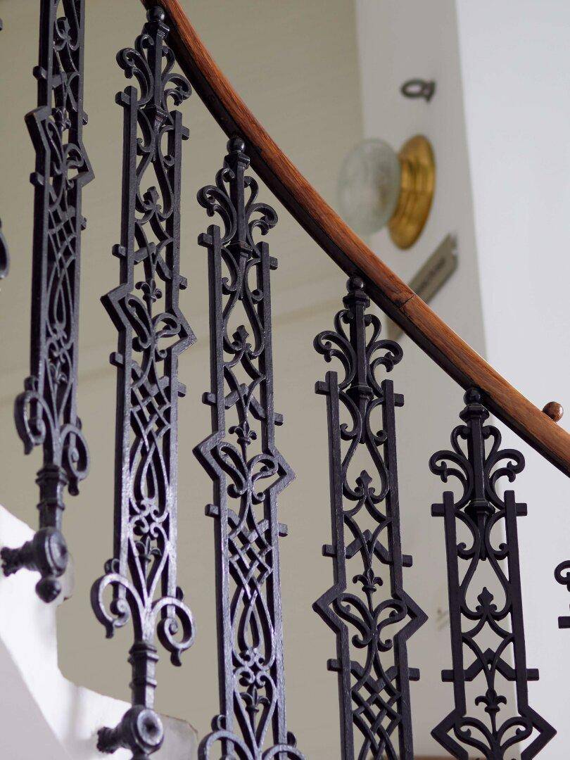 Detailansicht eines kunstvoll geschmiedeten Treppengeländers mit elegantem Holzhandlauf in einem Altbau.