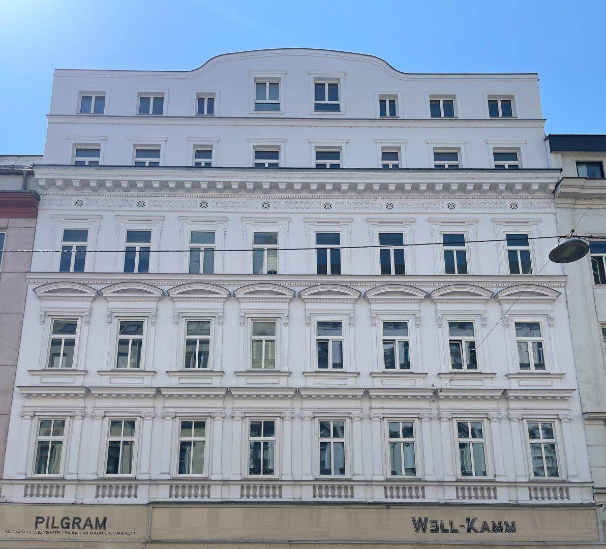 Historische Fassade eines Mehrfamilienhauses mit vielen Fenstern und dekorativen Elementen.