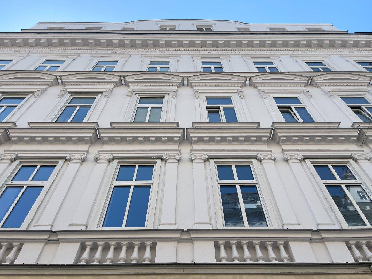 Detailansicht der eleganten Fassade eines Altbaus mit verzierten Fenstern und Balkongeländern.