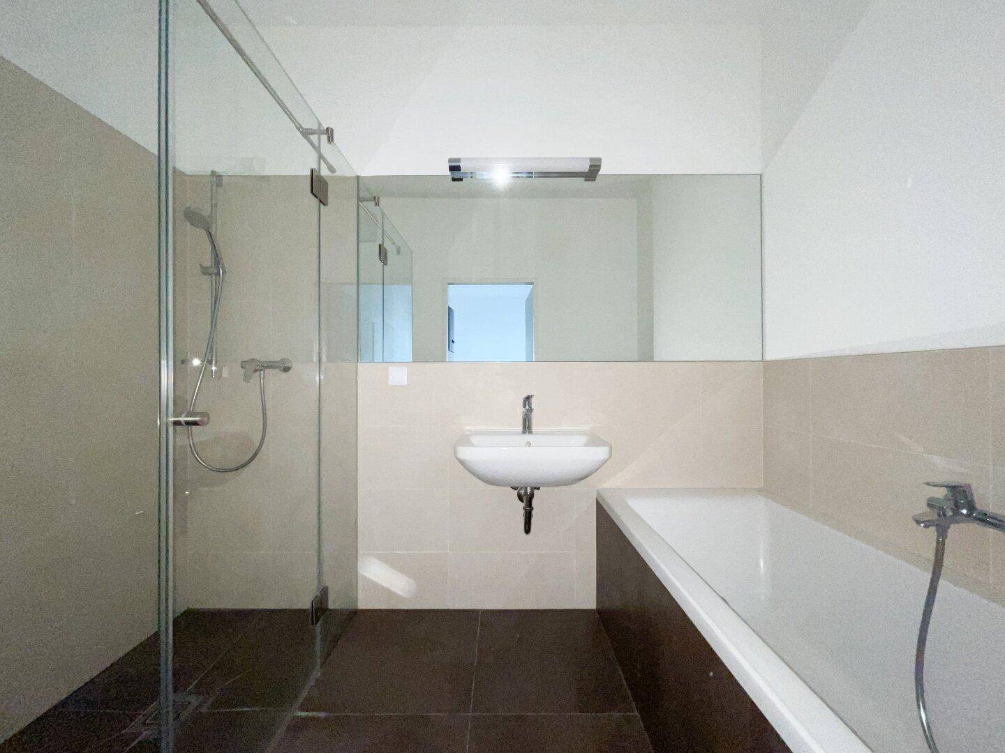 Modernes Badezimmer mit Badewanne, Dusche und großem Spiegel, in hellen und dunklen Fliesen.