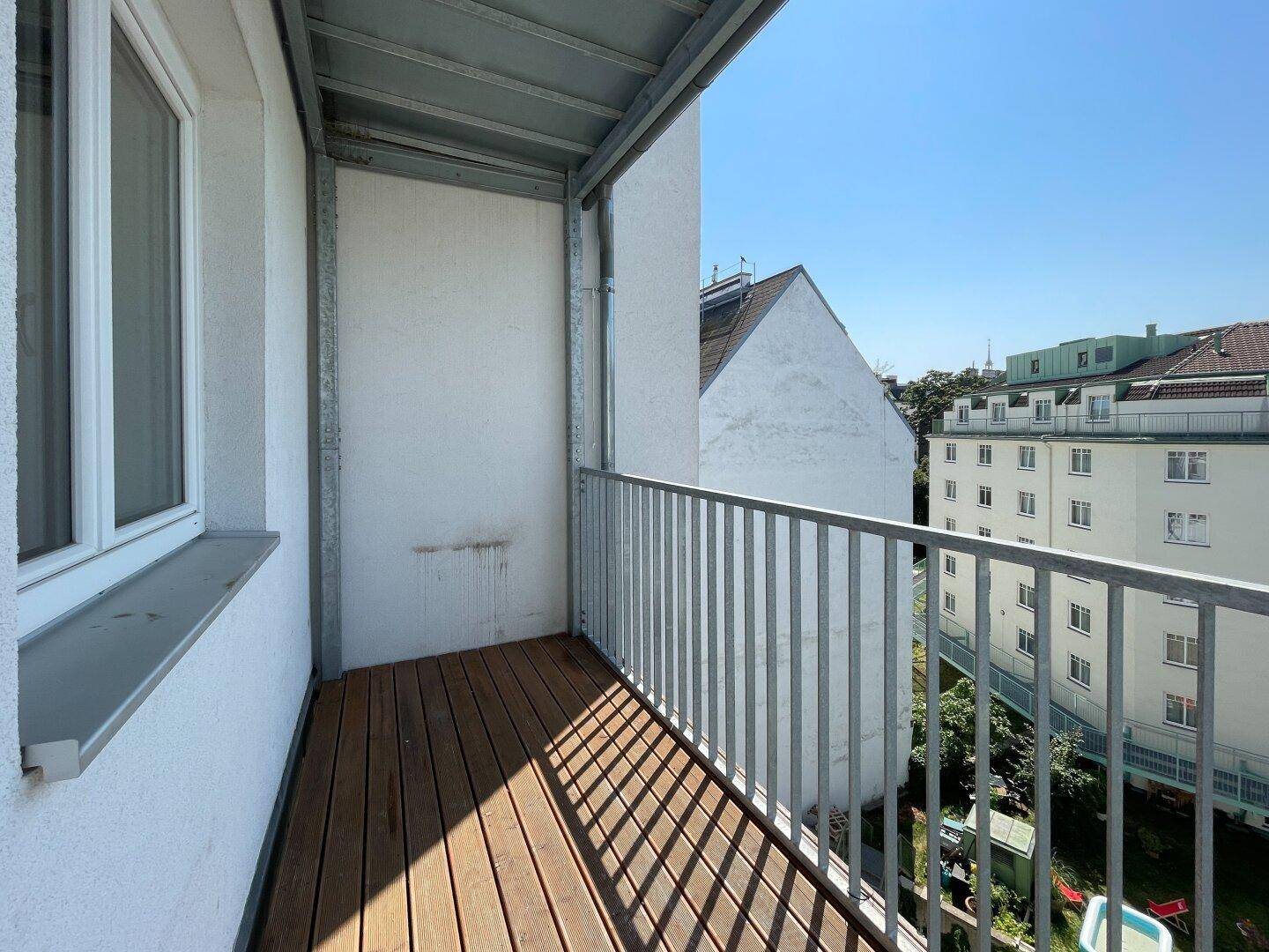 Kleiner Balkon mit Holzboden und Metallgeländer, bietet einen Blick auf die umliegenden Gebäude.