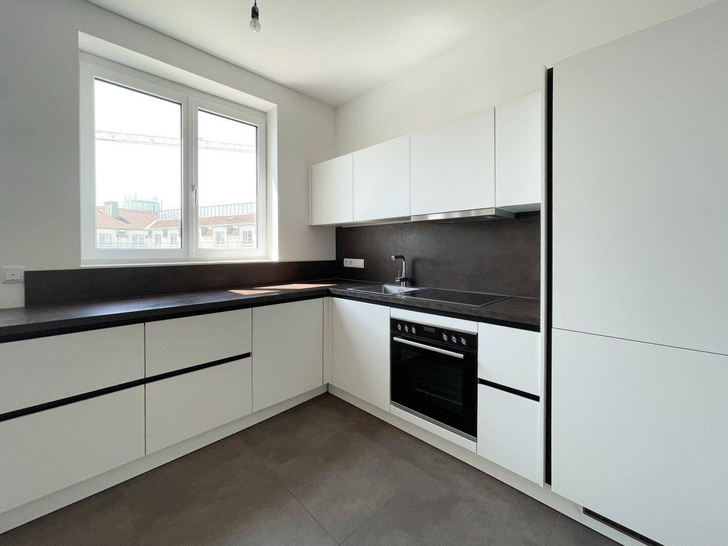 Moderne Einbauküche mit weißen Schränken, dunkler Arbeitsplatte und integrierten Geräten.