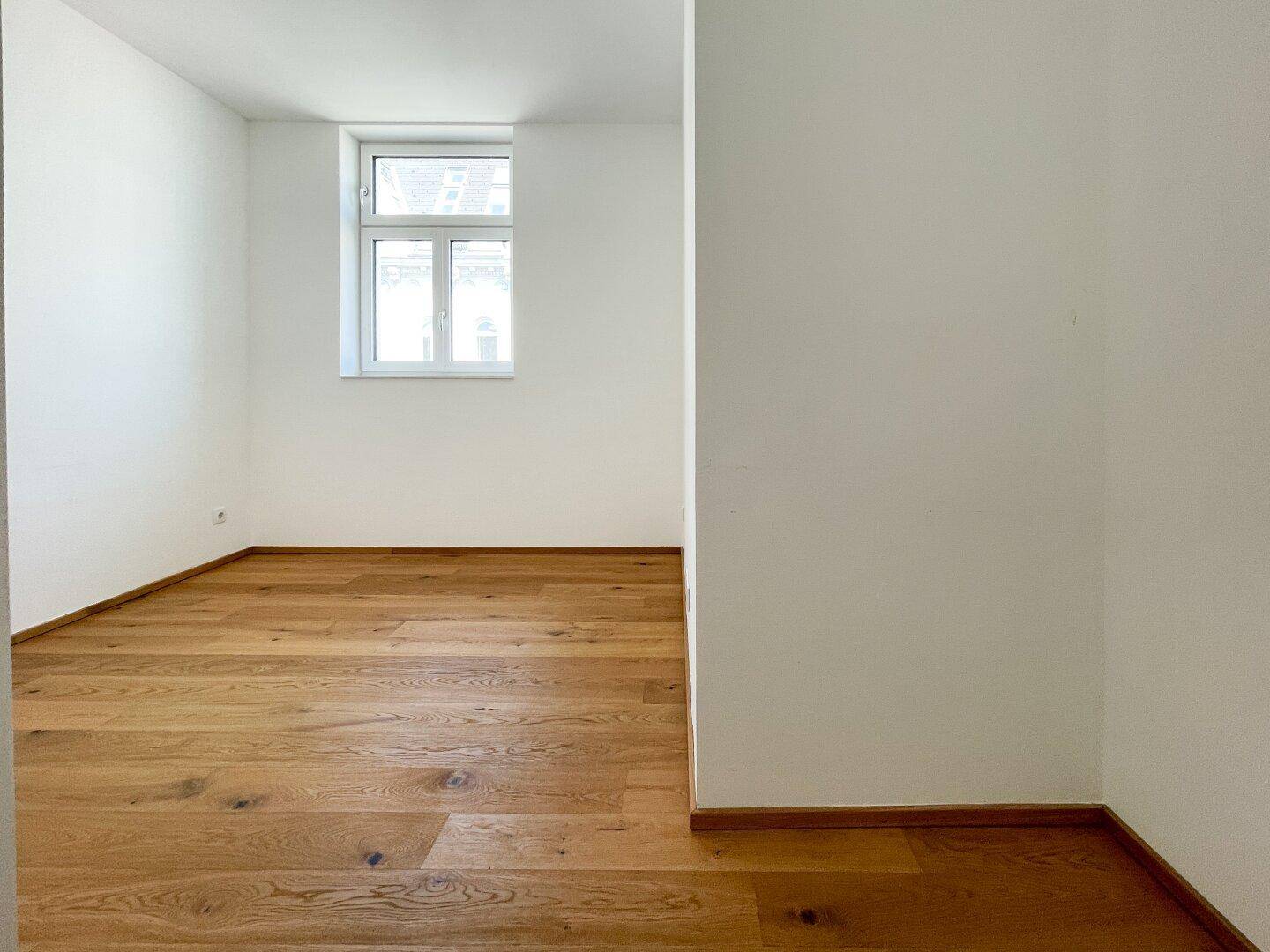 Helles Zimmer mit Holzboden und einem Fenster, das viel Tageslicht hereinlässt.