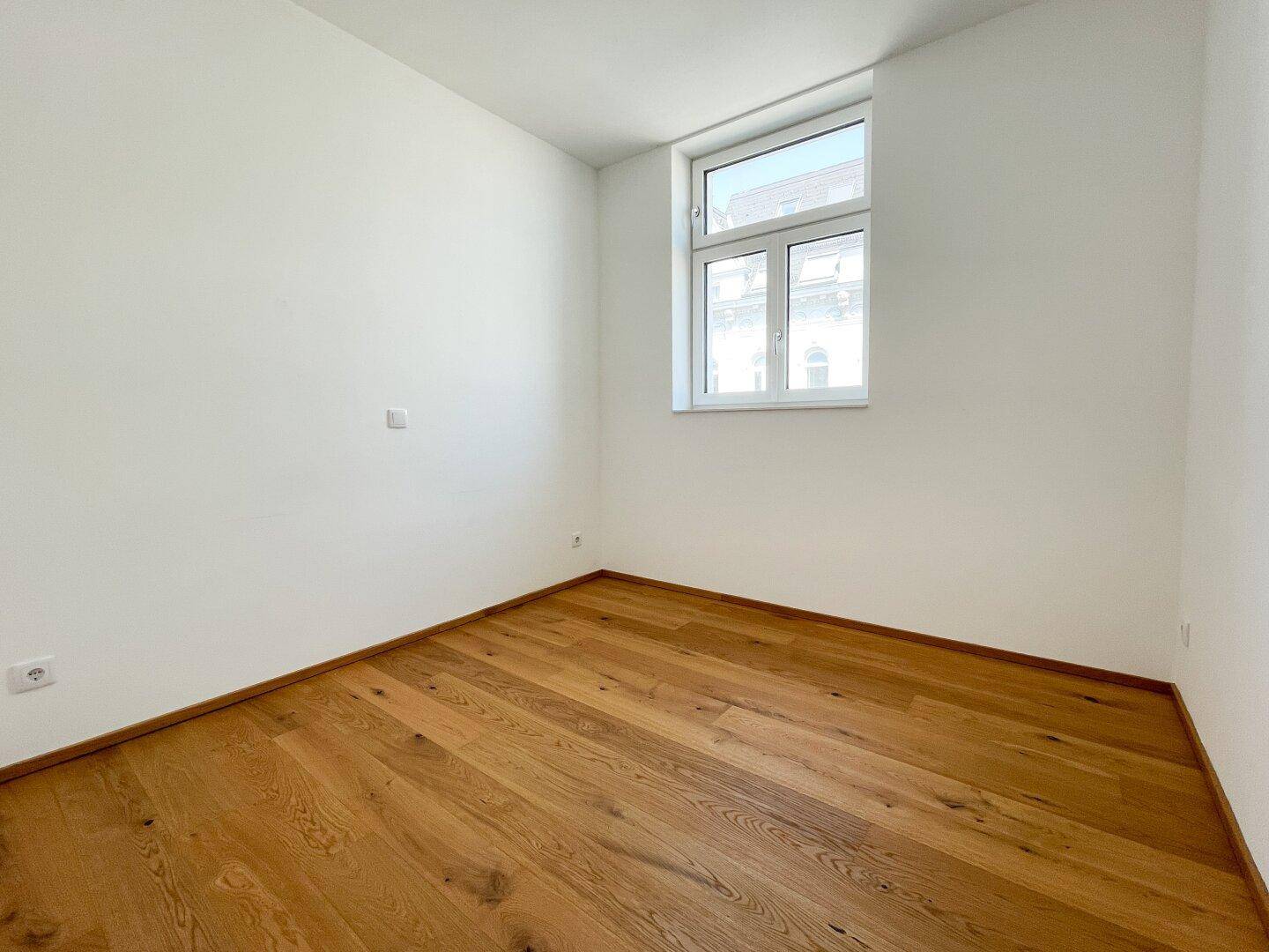Geräumiges Schlafzimmer mit hellem Holzboden und einem großen Fenster für natürliche Belichtung.