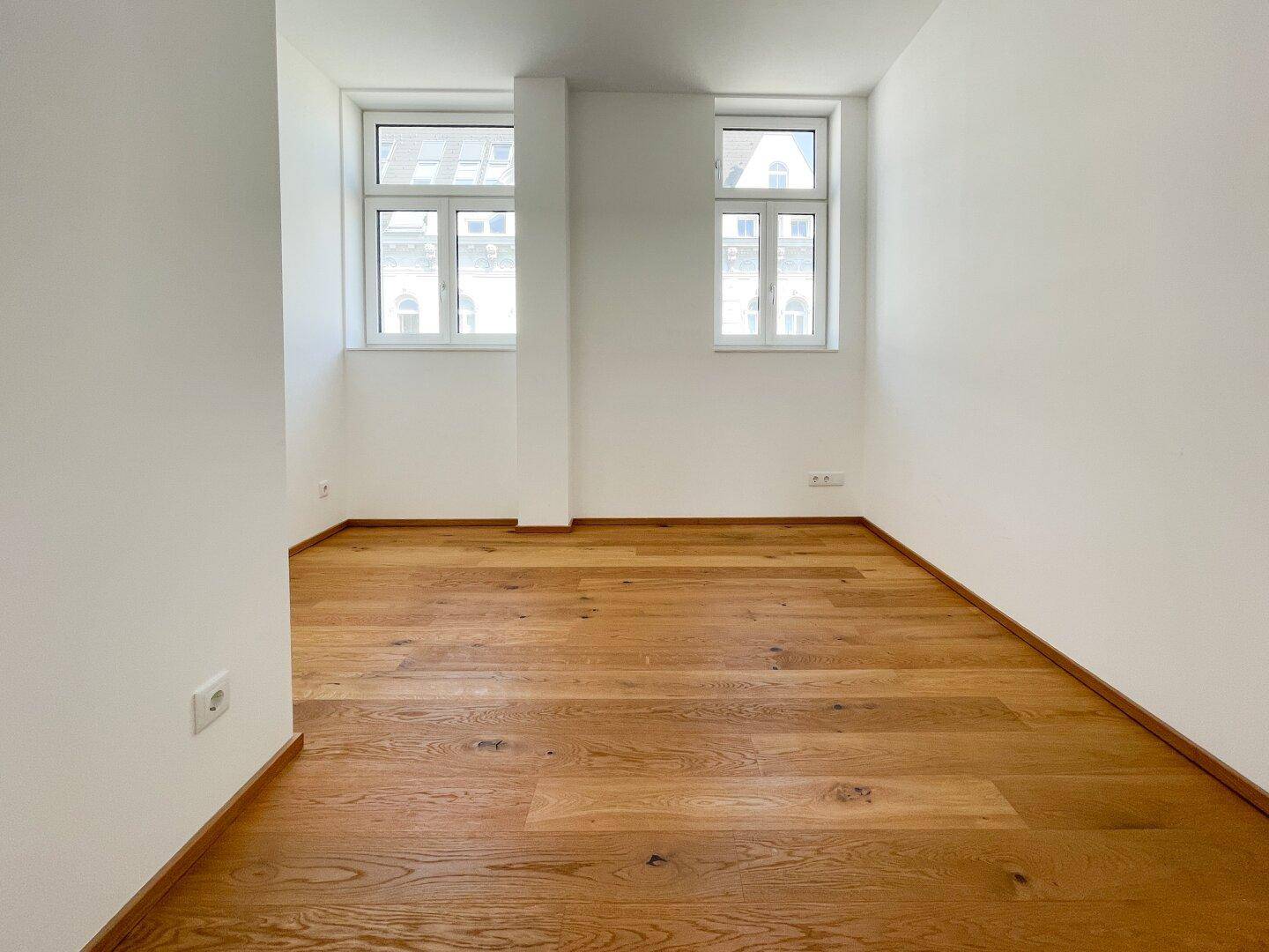 Freundliches Zimmer mit zwei Fenstern und Holzboden, ideal als Schlaf- oder Arbeitszimmer.