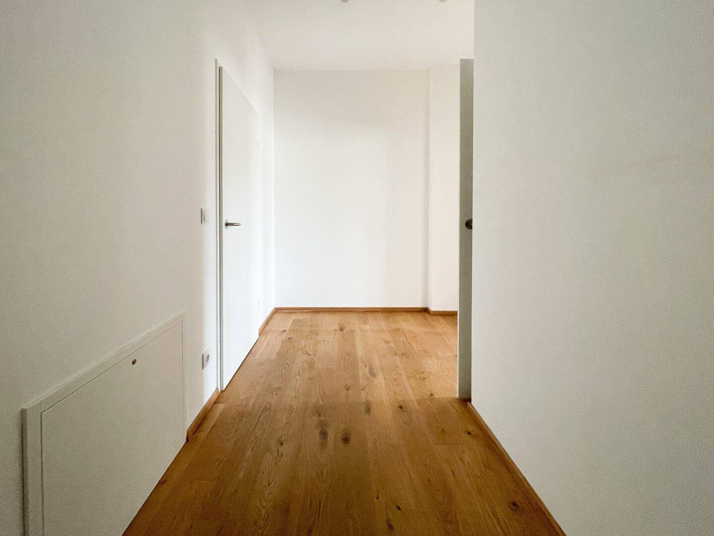 Langer, heller Flur mit Holzboden und weißen Wänden, der verschiedene Räume verbindet.