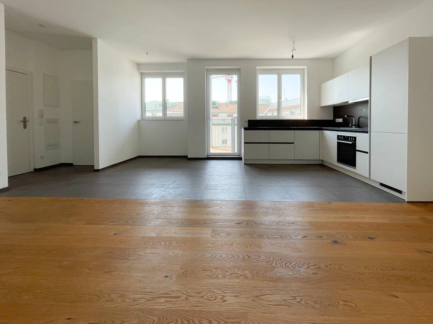 Offener Wohnbereich mit moderner Küche, Holzboden und Zugang zu einem kleinen Balkon.