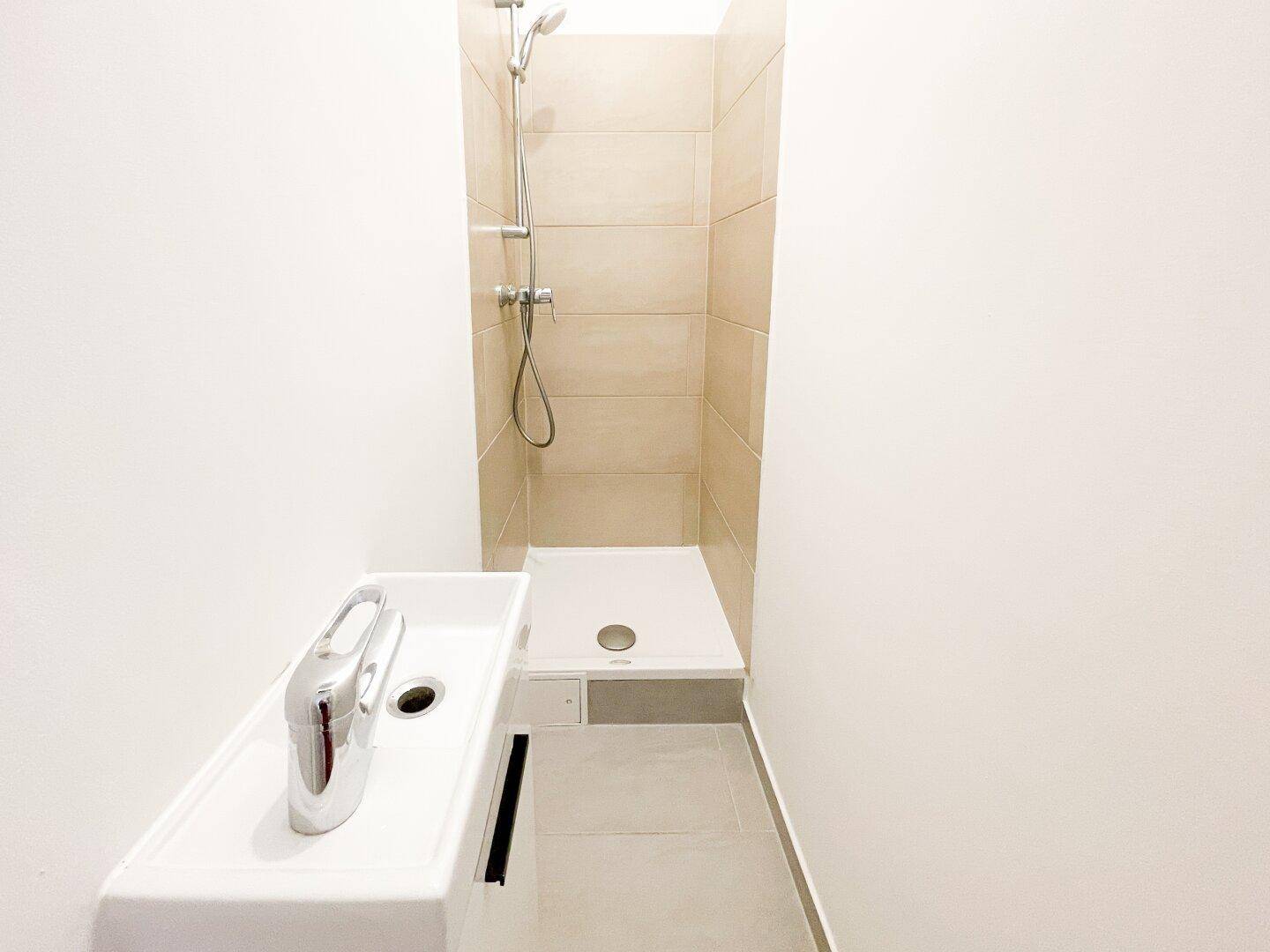 Kompaktes Badezimmer mit Duschbereich und modernem Waschbecken in hellen Fliesen.