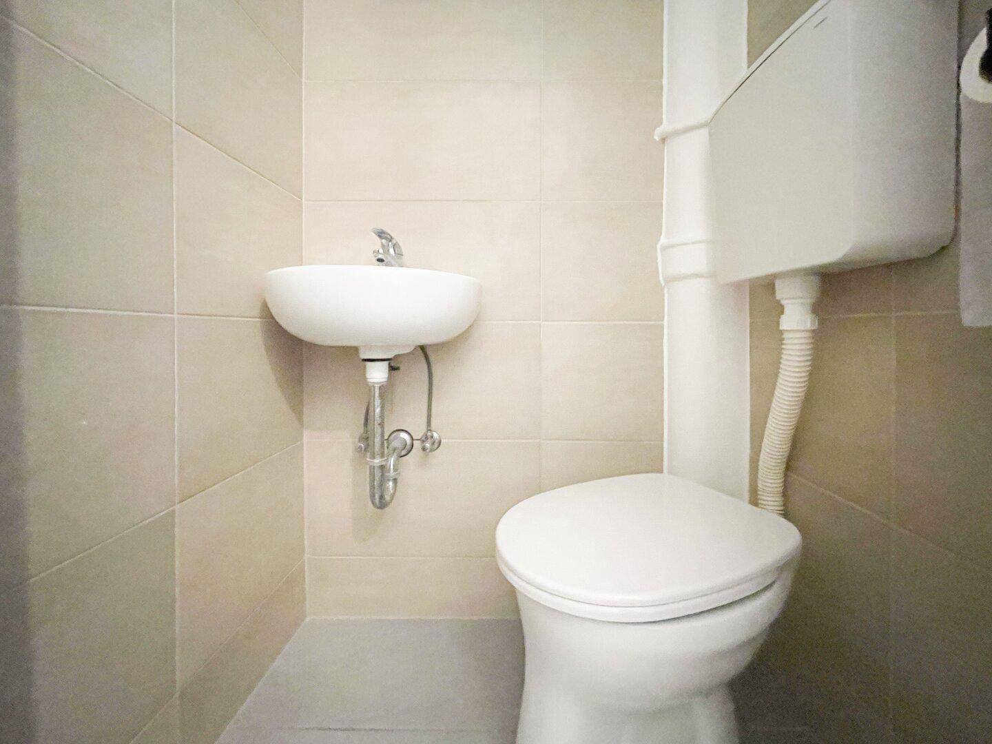 Kleines Gäste-WC mit wandmontiertem Waschbecken und Toilette in neutralen Fliesen.