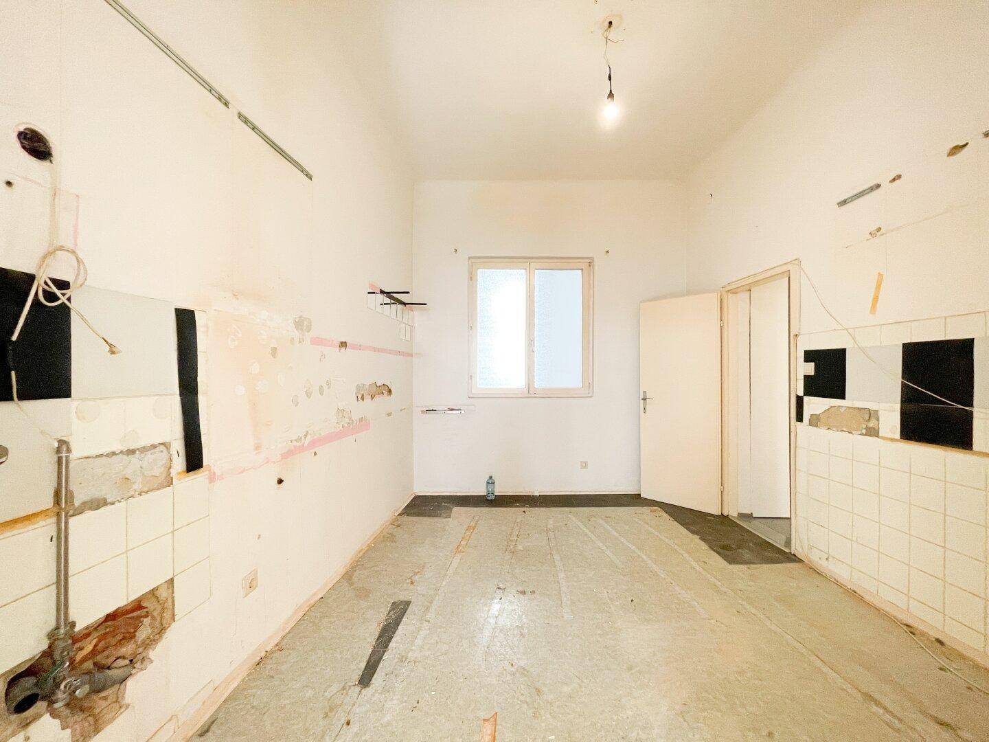 Renovierungsbedürftige Küche mit Fenster und alten Fliesen, bereit für eine Neugestaltung.