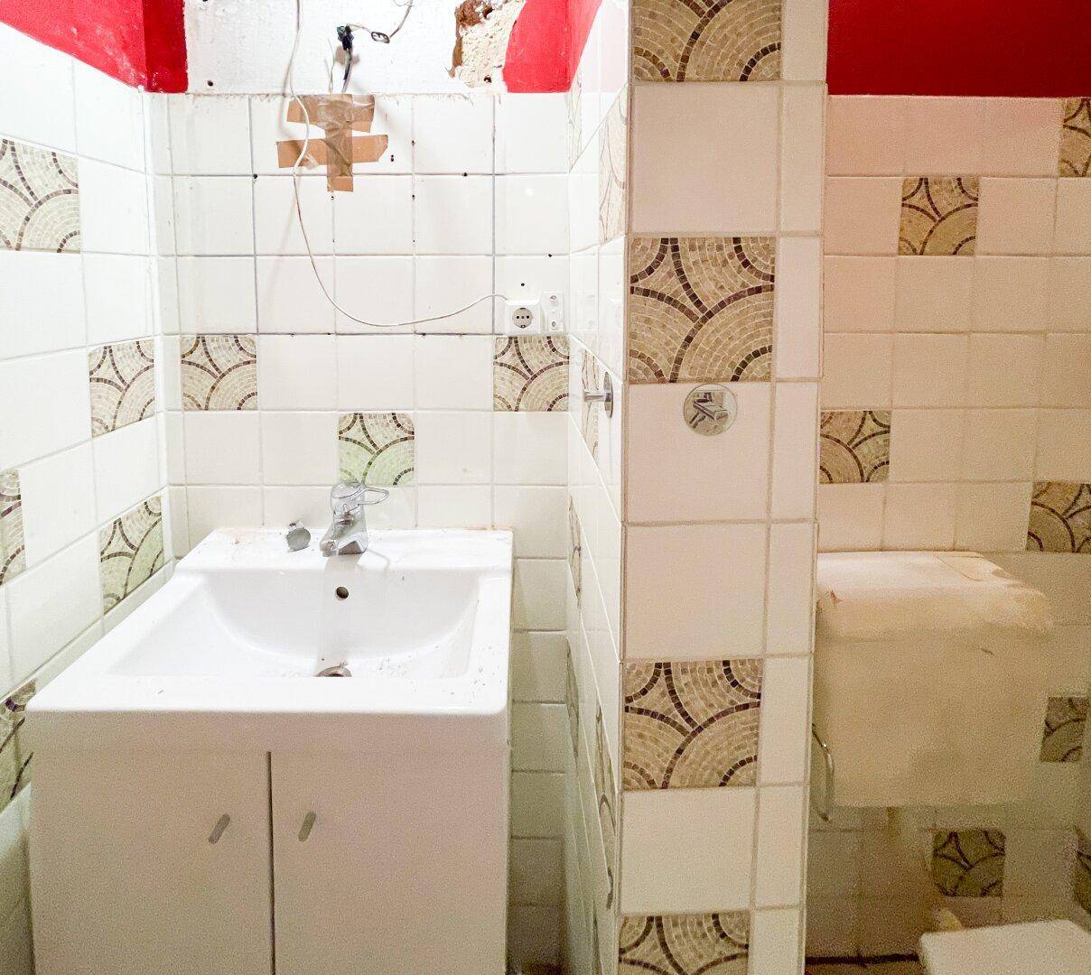 Kleines Badezimmer mit Waschbecken und Toilette, umgeben von gemusterten Wandfliesen.