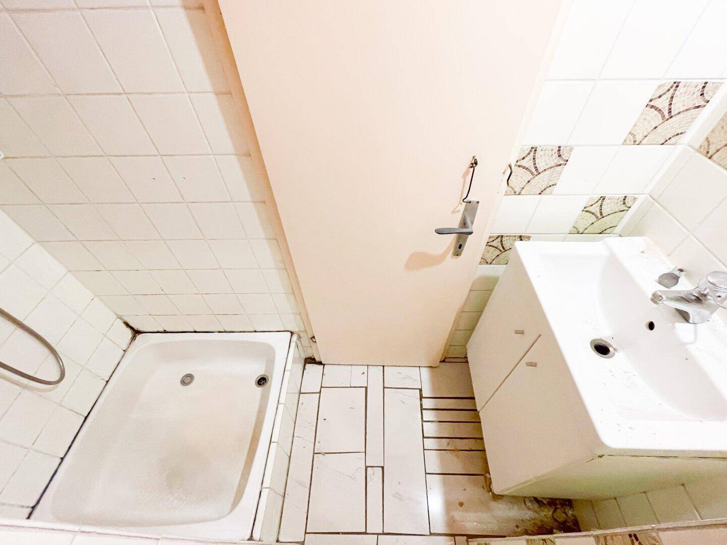Kleines Badezimmer mit Badewanne und Waschbecken, umgeben von weißen Fliesen.