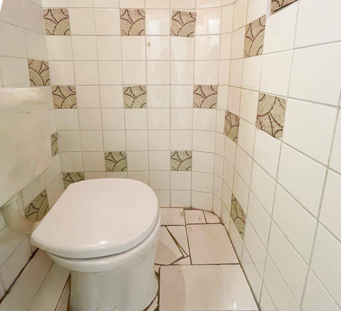 Toilette in einem kleinen Raum mit gemusterten Fliesen, bereit für eine Modernisierung.