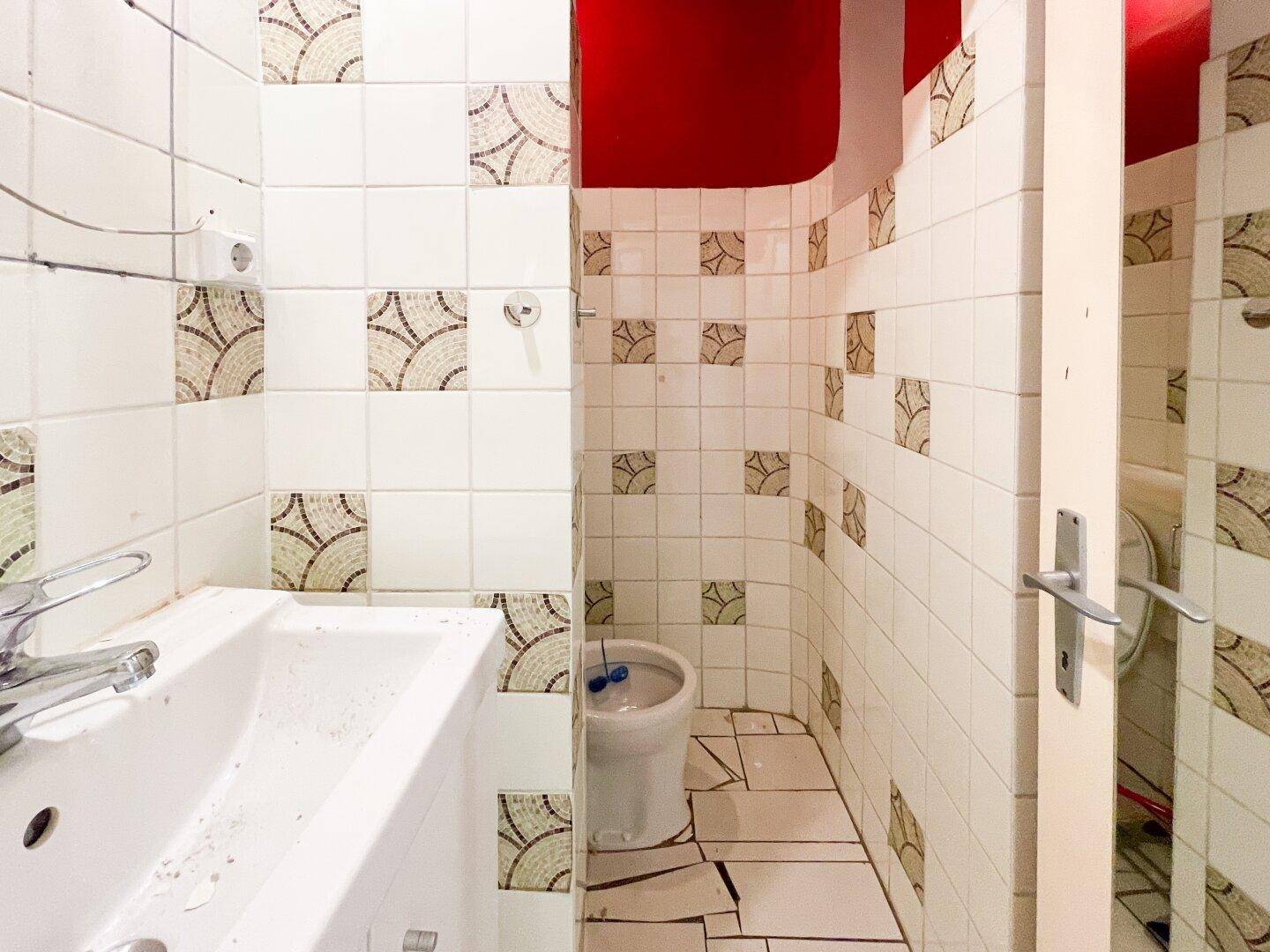 Kleines Badezimmer mit Waschbecken, Toilette und gemusterten Fliesen, renovierungsbedürftig.